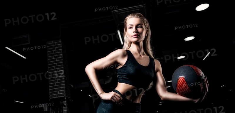 Charming blonde posing in the gym with a fitness ball. Front view. The concept of sports