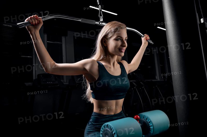 Charming blonde does exercises for the back in the gym. Neck pull for the head. The concept of sports