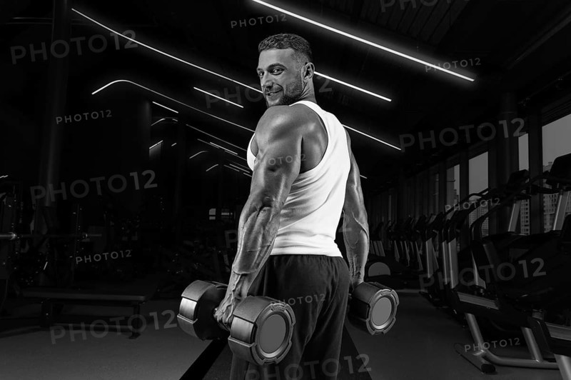 Handsome young man working out with dumbbells in the gym. Shoulder pumping. Fitness and bodybuilding concept.