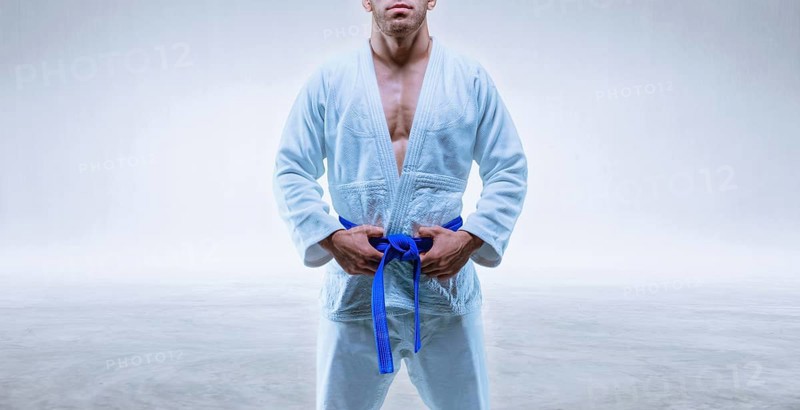 Athlete in a kimono with a blue belt stands on a light background. The concept of karate and judo.