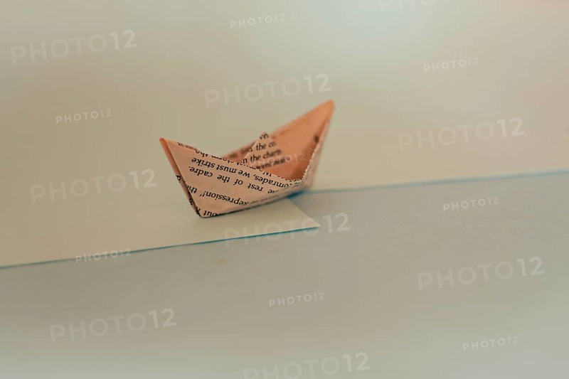 An origami paper boat with a minimalist design casting a shadow on a blue surface