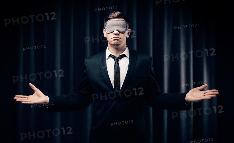 Portrait of a man in a mask for sleeping. He stands against the backdrop of a curtain. The concept of blind dates