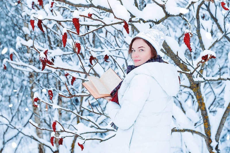 Portrait of a charming girl who reads a book in the winter forest. Concept of Christmas