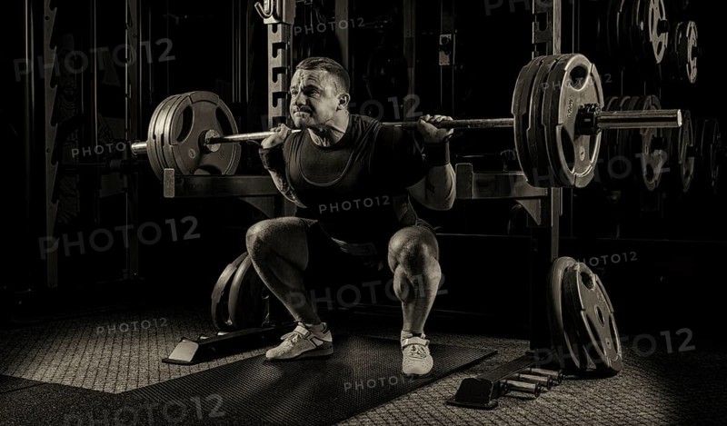 The weightlifter is getting ready to stand with a heavy barbell. Is at the bottom point