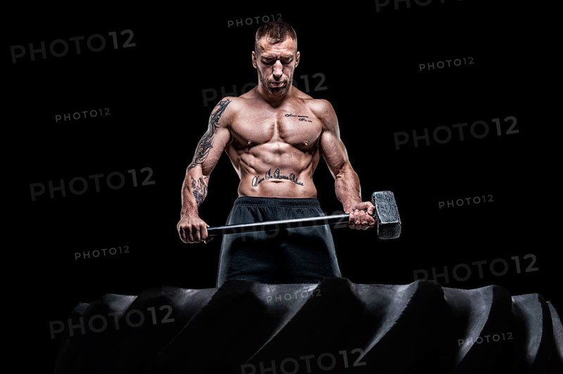 Professional sportsman stands with a sledgehammer in front of a rubber wheel. Functional training concept.