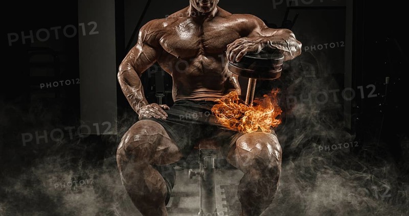 Muscular man sits on a bench with dumbbells burning. Bodybuilding and powerlifting concept.