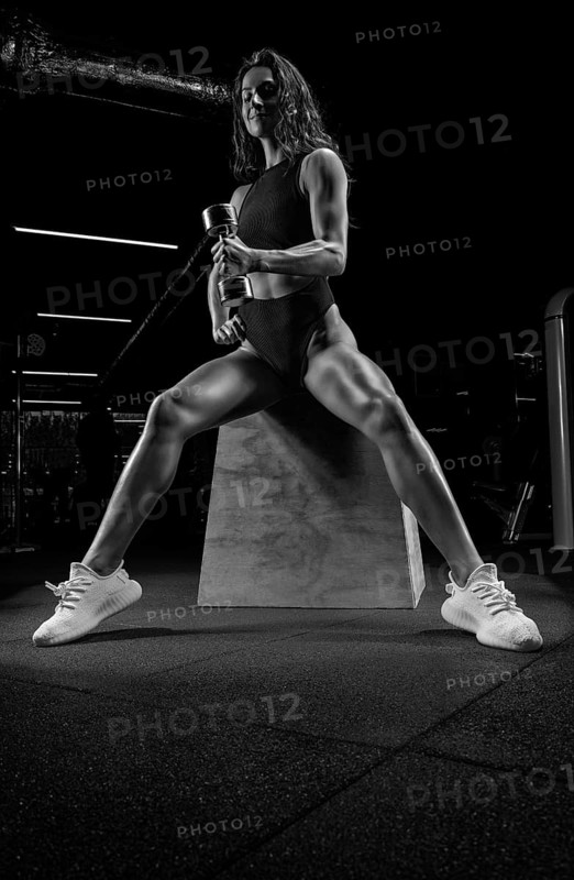 Tall athletic woman posing in the gym on a bench with dumbbells. Biceps pumping. Fitness and bodybuilding concept.