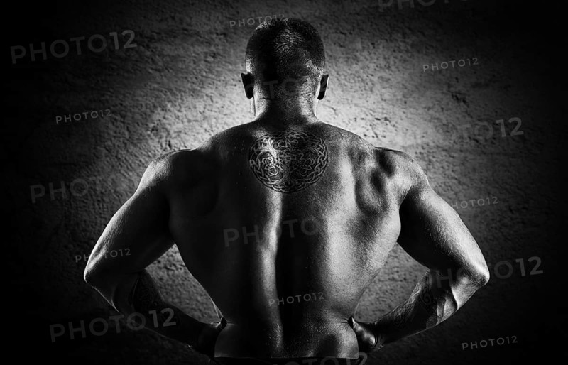 Huge weightlifter stands with his back to the camera and shows his huge back. Back view