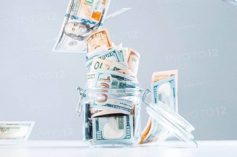 Glass piggy bank full of money. Banknotes are strewed from above. The concept of squandering.