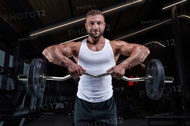 Handsome young man working out with a barbell in the gym. Shoulder pumping. Barbell pull to the chin. Fitness and bodybuilding concept
