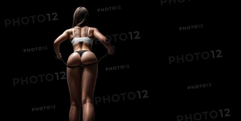 Young and sexy girl posing with a skipping rope in the studio. Back view. Sports concept.