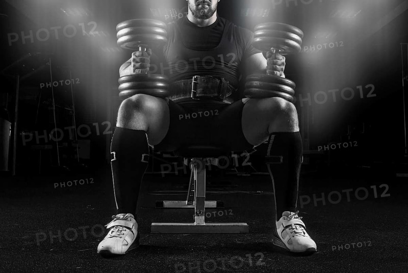 Professional weightlifter sits on a bench in the gym with two dumbbells on his lap