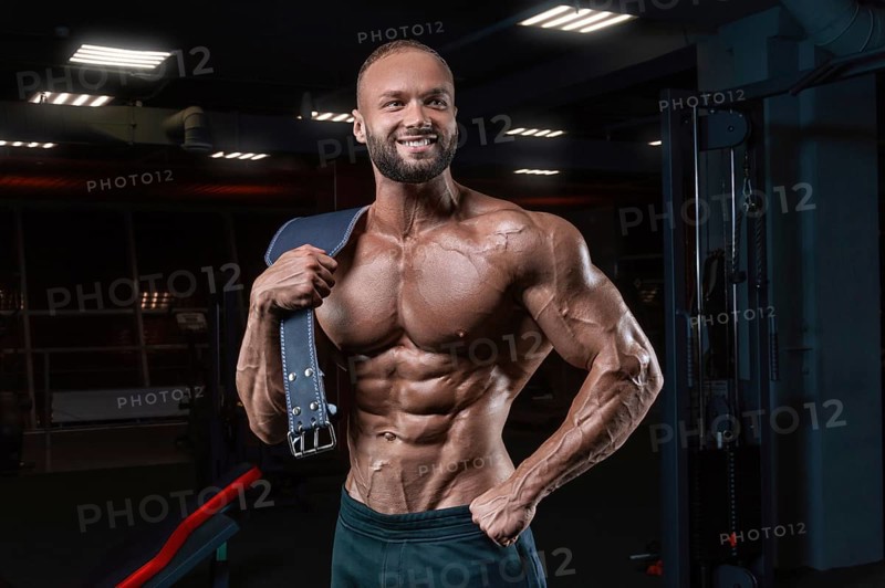 Muscular man poses in the gym with an athletic belt. Sports