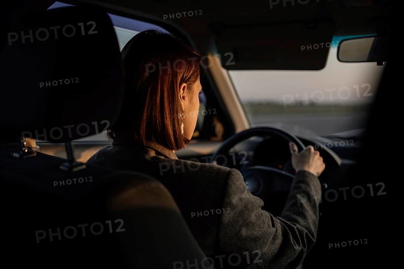 Young beautiful smiling woman taxi driver in a jacket sits behind the wheel of a car