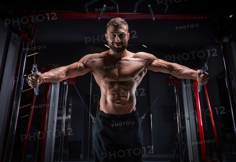 Muscular athlete training in a crossover at the gym. Pumping the torso. Fitness and bodybuilding concept.