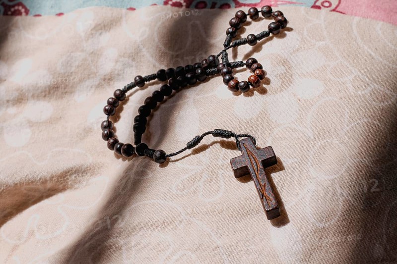 A rosary with a cross lying on a fabric surface in a softly lit environment