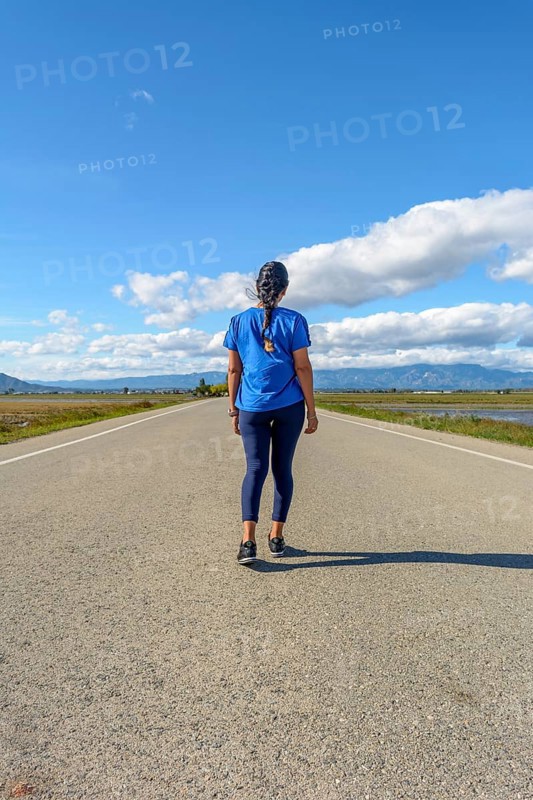 A traveler in casual attire treading along a paved road towards the horizon in a serene setting
