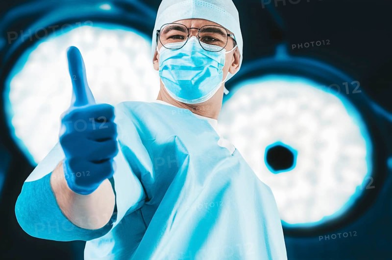 The doctor against the background of surgical lamps shows a raised finger. Medicine concept.