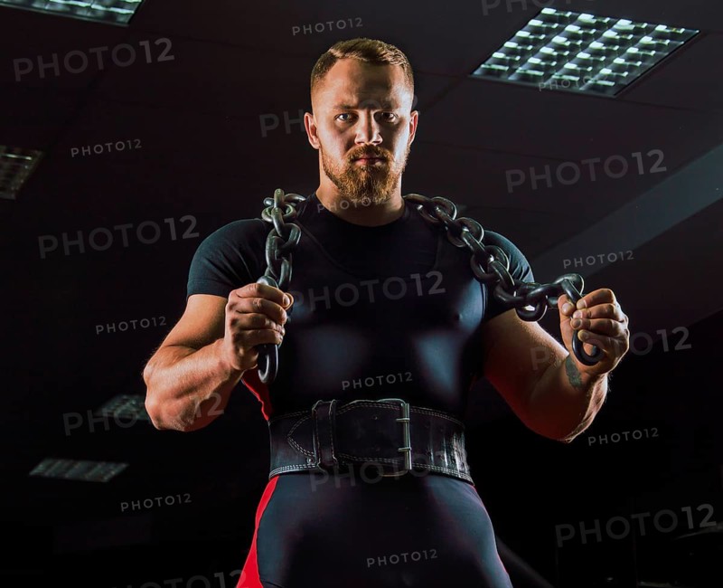Huge weightlifter with a chain around his neck is in the gym