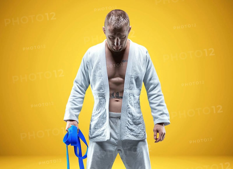 Strong man in a kimono with a blue belt. Yellow background. Martial arts concept.