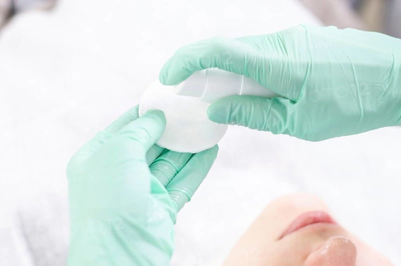 Image of hands in green gloves holding a spray bottle and cotton pads. Skin care concept.