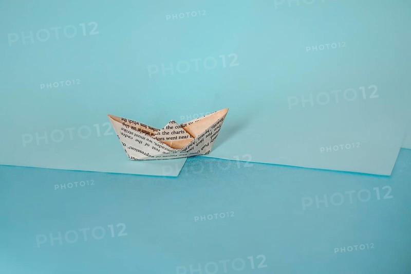 An origami paper boat on a two-tone background casting a long shadow