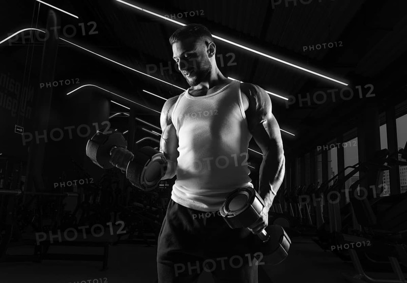 Muscular man in a white t-shirt works out in the gym with dumbbells. Biceps pumping. Fitness and bodybuilding concept.