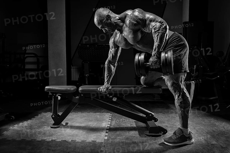 Muscular man pulls a dumbbell towards his stomach. Bodybuilding and powerlifting concept.