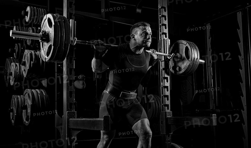 The weightlifter is preparing to lift a very heavy barbell. He exhales breathlessly and strains as much as possible before performing the exercise