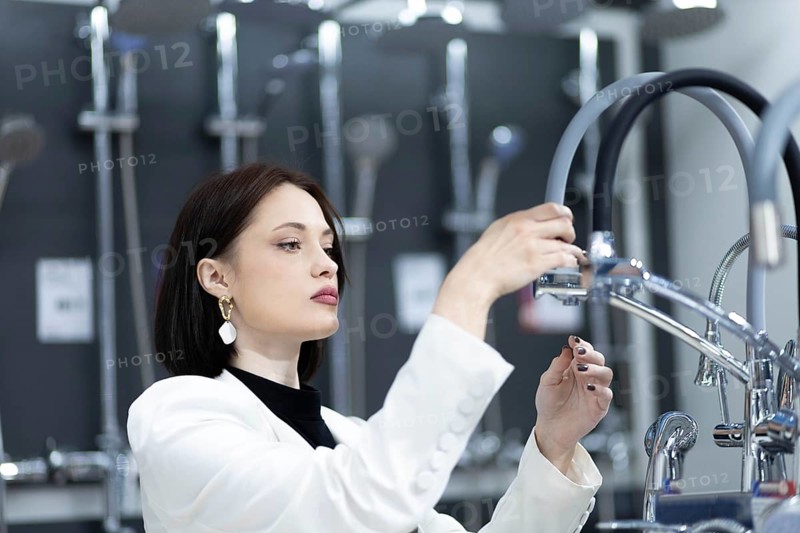 Beautiful young woman in a white jacket chooses plumbing supplies in a hardware store