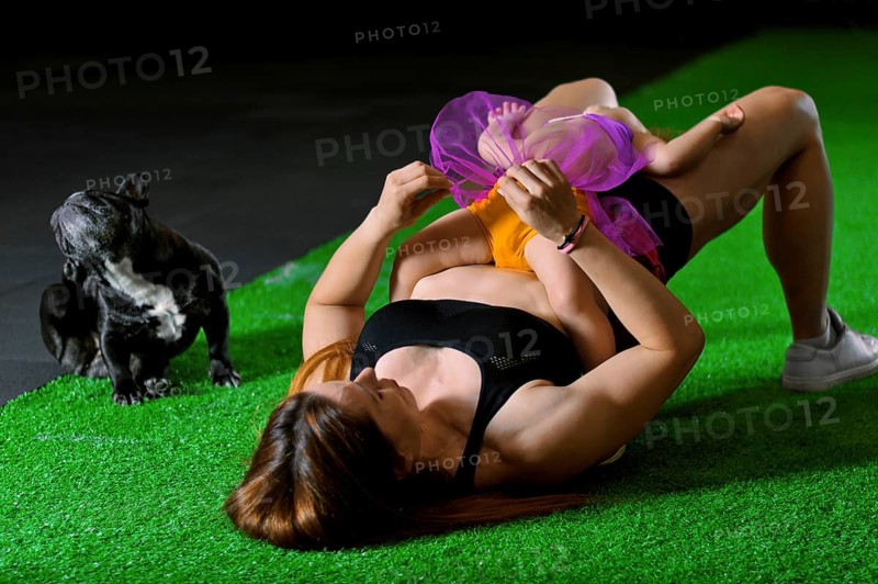 Charming sports mom plays in the gym with her little daughter and a French bulldog.