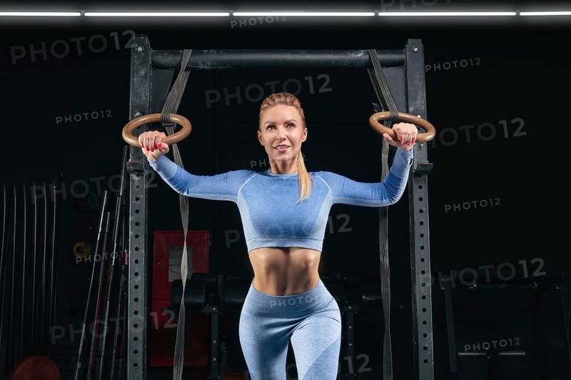 Beautiful tall blonde is training on athletic rings. Fitness and bodybuilding concept.