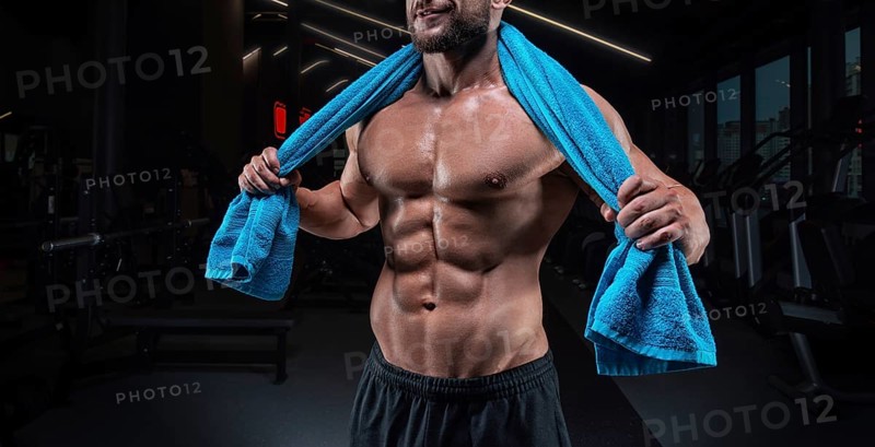 Muscular man posing in the gym with a towel on his shoulders. Fitness concept.