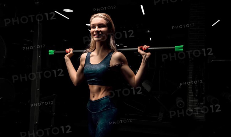 Charming blonde posing in the gym with a body-bar. Front view. The concept of sports