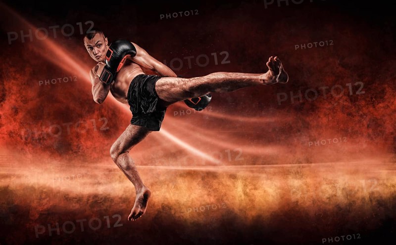 Professional kickboxer jumps with his knee extended. Fiery arena. Mixed martial arts. Sports concept