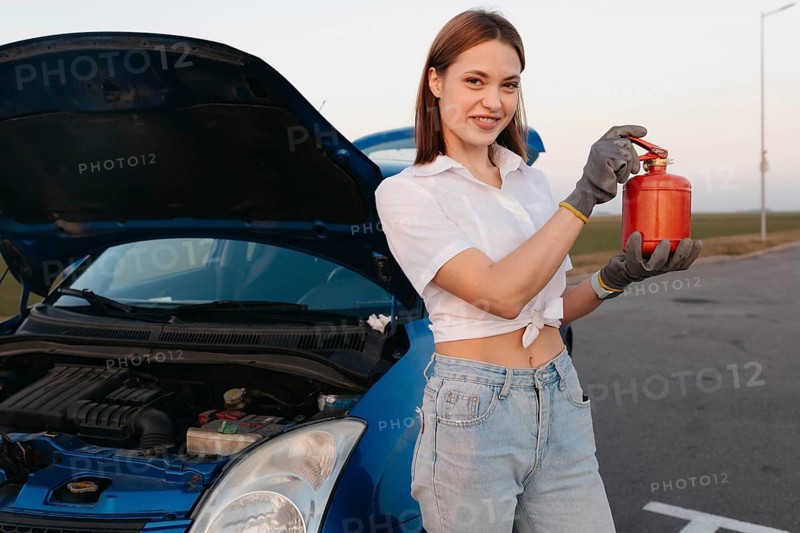 Young beautiful and hot woman driver holds a fire extinguisher in her hands