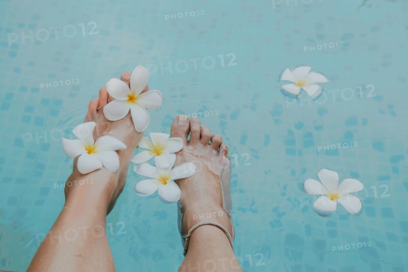 Feet adorned with plumeria flowers by a blue swimming pool