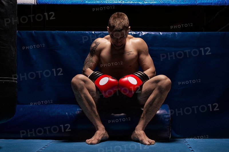 Boxer sits in gloves near the ring with his head bowed. The concept of sports