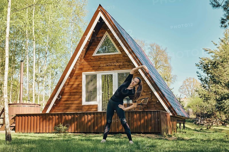 Sporty woman does side body bent on lawn of a log cabin in the morning