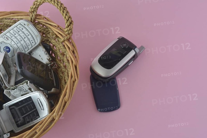 An open flip cell phone in the foreground with more phones in a basket behind