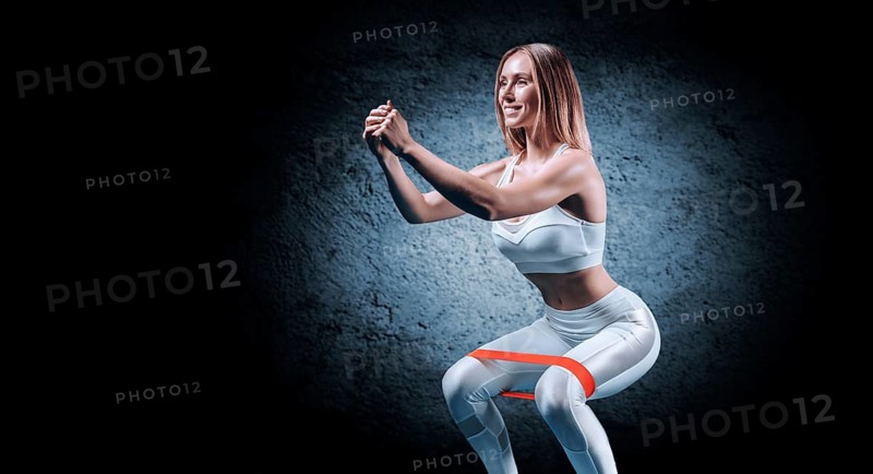 Charming girl is training in the gym with a rubber band. The concept of bodybuilding