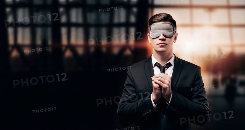 Man in a business suit and a mask for sleeping is standing at the airport. He is praying. Airline concept. Caring for passengers.