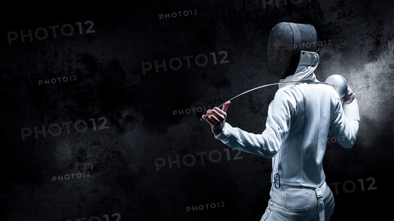 Charming girl dressed as a fencer posing with a mask and a sword. The concept of fencing. Back view.