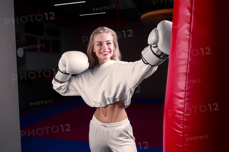 Cheerful and charming girl in a white sweatshirt boxing in huge gloves and smiling. The concept of sports