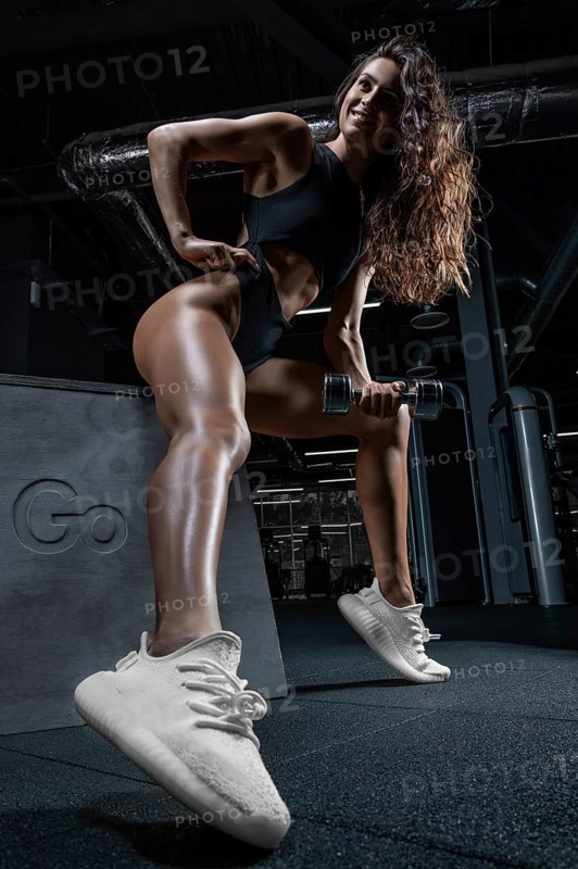 Tall athletic woman posing in the gym on a bench with dumbbells. Biceps pumping. Fitness and bodybuilding concept.
