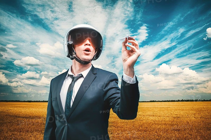 Portrait of a man in a helmet of a pilot. He stands in a field and launches a paper airplane. Business concept.