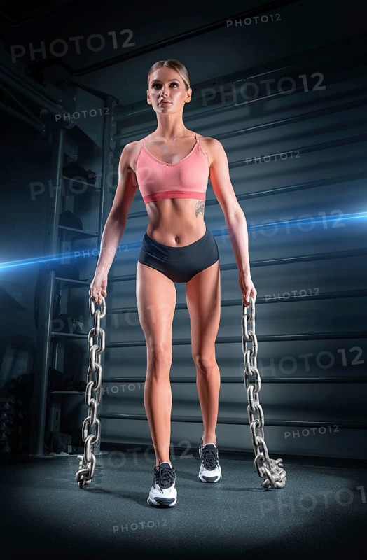 Sports girl trains in the gym against the background of the wall bars. She carries heavy metal chains in her hands. The concept of sports