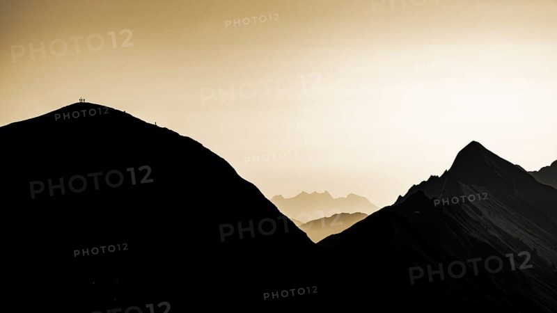 Mountain ridge with mountaineers and Swiss mountains and Lake Thun in the background at sunrise