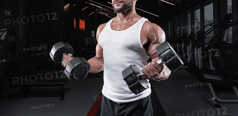 Portrait of a man in a white T-shirt exercising in the gym with dumbbells. Biceps pumping. Fitness and bodybuilding concept.
