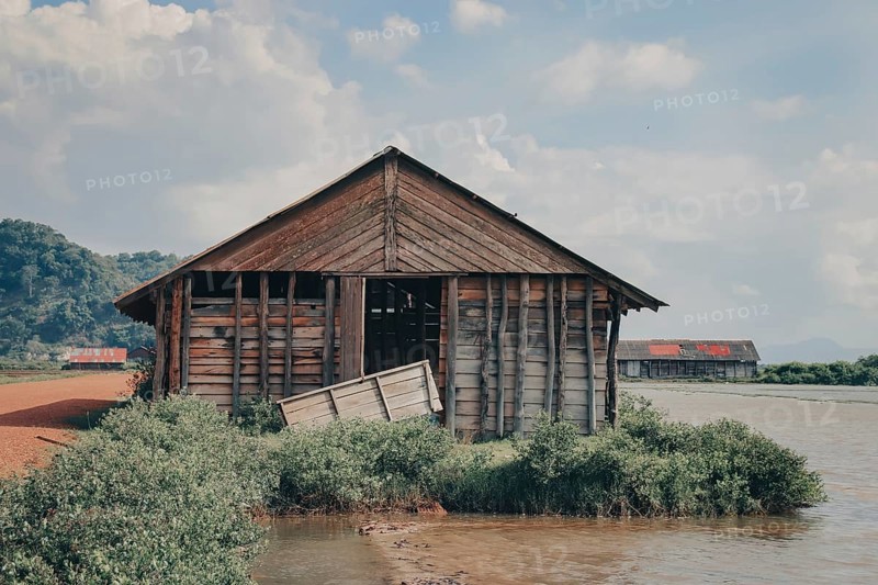 Derelict wooden shack on the riverbank surrounded by greenery. Kampot